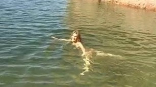 Cute young brunette strips by the water and goes skinny dipping